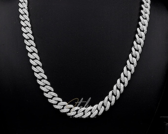 Könnte beinhalten: Eine silberfarbene Cuban-Link-Kette mit zahlreichen kleinen, klaren Steinen. Die Halskette wird auf einer schwarzen Mannequin-Büste präsentiert. Die Kettenglieder sind eng miteinander verbunden und erzeugen ein durchgehendes, funkelndes Aussehen. Der Hintergrund ist schwarz.