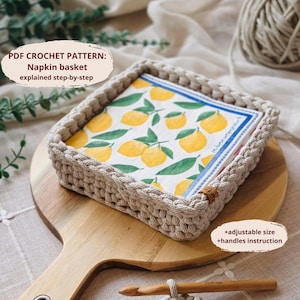 May include: A crocheted napkin basket with a square shape, filled with lemon-printed napkins. The basket is beige and sits on a wooden cutting board. Text on the image reads "PDF CROCHET PATTERN: Napkin basket explained step-by-step".