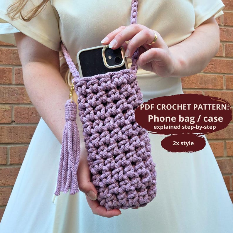 May include: A lilac crochet phone bag with a matching strap and tassel. The bag is designed to hold a smartphone and is shown being held by a person. The text on the image says "PDF CROCHET PATTERN: Phone bag / case explained step-by-step 2x style."