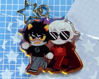 May include: A clear acrylic keychain featuring two cartoon characters. One character has black hair and a black shirt with the number 69. The other character has white hair and wears sunglasses and a red outfit. The keychain has a star-shaped clasp.