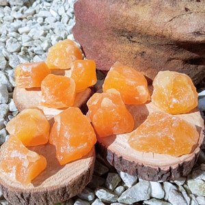 Peut inclure: Une collection de cristaux de calcite orange sur une surface en bois. Les cristaux sont de différentes tailles et formes, certains ayant une texture rugueuse.