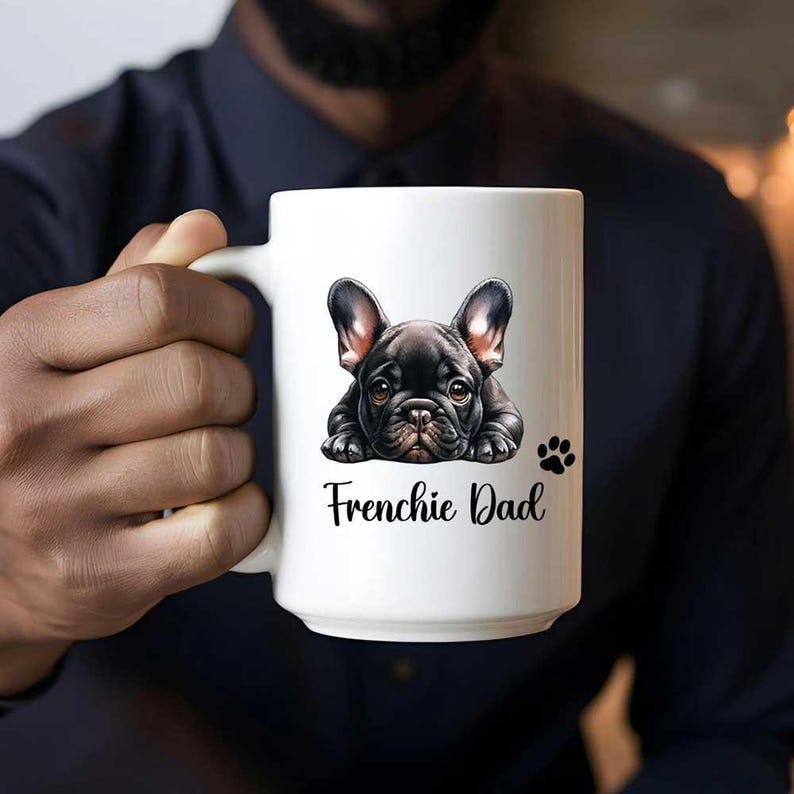 A 15oz white mug watercolor black French Bulldog mug with a paw and a text says Frenchie Dad. The French Bulldog is lying on the floor with a puppy eye look.