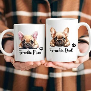 Left mug shows a Fawn French Bulldog with pink color ears while on the right mug shows a Fawn French Bulldog with fawn color ears. Left mug says Frenchie Mom and Right mug says Frenchie Dad with a paw print.