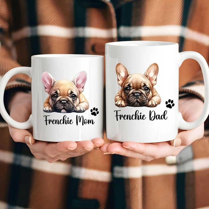 Left mug shows a Fawn French Bulldog with pink color ears while on the right mug shows a Fawn French Bulldog with fawn color ears. Left mug says Frenchie Mom and Right mug says Frenchie Dad with a paw print.