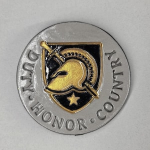 May include: A round, silver-colored coin with the words "DUTY HONOR COUNTRY" embossed around the edge. The center features a black and gold shield with a helmet, sword, and star.