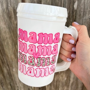 May include: White travel mug with a pink and black design that says "mama mama mama mama" with hearts.