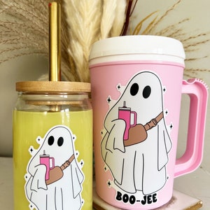 May include: Two glass mugs with a ghost holding a pink drink and the text "BOO-JEE" on the front. The mugs are yellow and pink and have a wooden lid.