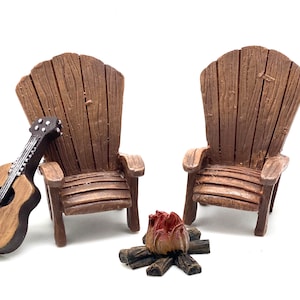 May include: Two brown wooden adirondack chairs with a small campfire and a brown acoustic guitar in front of them.