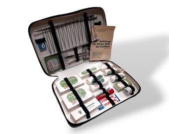 May include: A black leather first aid kit with a white zipper and a white interior. The kit is open and contains various medical supplies, including bandages, gauze, antiseptic wipes, and a pair of tweezers. The kit also includes a small booklet titled "Anleitung zur Ersten Hilfe bei Unfallen".