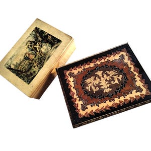 Op de afbeelding: Twee antieke houten dozen. Eén is een klein boek met een vervaagde illustratie op de omslag. De andere is een rechthoekige doos met een donkerbruin en beige bloemenontwerp en een decoratief midden.