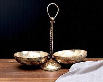 May include: A silver serving dish with two bowls and a handle. The bowls are round and have a decorative pattern. The handle is ornate and has a beaded design.