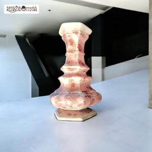 Può includere: Un vaso in ceramica bianca con una glassa rosa e bianca. Il vaso ha una base esagonale e un corpo arrotondato con una parte superiore svasata.
