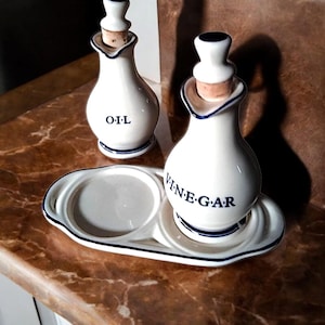 Op de afbeelding: Witte keramische olie- en azijnflessen met kurken stoppen en blauwe rand. De flessen staan op een bijpassend dienblad. Het woord "OIL" staat op de ene fles en "VINEGAR" op de andere. Een klassieke keukenset.