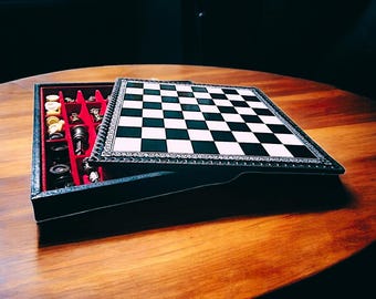 May include: A black leather chessboard set with a white and black checkered board and silver accents. The set is open and the pieces are visible in the compartments.