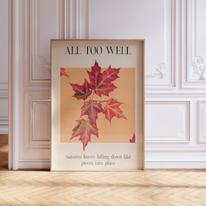 May include: A framed poster with the text "ALL TOO WELL" and a picture of red maple leaves. The text below the image reads "Autumn leaves falling down like pieces into place."
