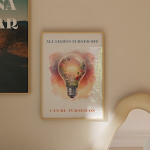 May include: A framed print with a watercolor illustration of a light bulb with a garden inside. The text "ALL LIGHTS TURNED OFF CAN BE TURNED ON" is printed below the image.