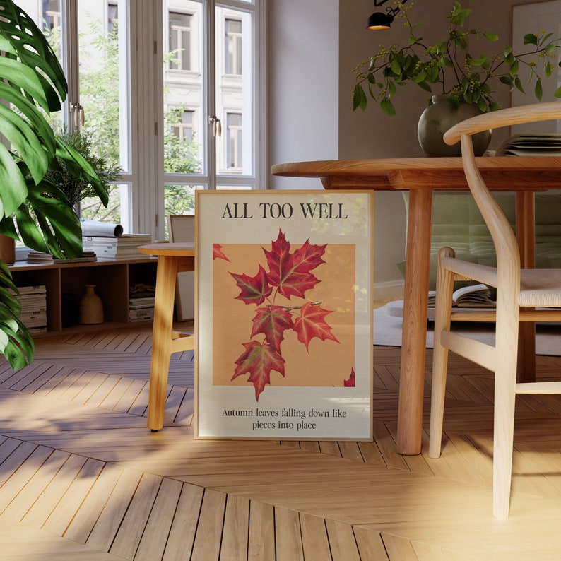 May include: A framed print with the text "All Too Well" and a picture of red and orange autumn leaves falling down. The text below the image reads "Autumn leaves falling down like pieces into place."