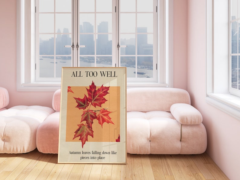 May include: A framed poster with the text "ALL TOO WELL" and a picture of red maple leaves against a light orange background. The text below the image reads "Autumn leaves falling down like pieces into place."