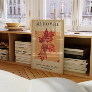 May include: A framed print with the text "ALL TOO WELL" and a vintage illustration of red maple leaves. The text below the image reads "Autumn leaves falling down like pieces into place."