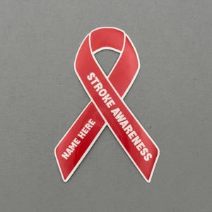 May include: A red ribbon with white text that reads "STROKE AWARENESS" and "NAME HERE". The ribbon is a symbol of awareness and support for stroke survivors and their families. The ribbon is on a gray background.