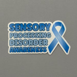May include: A rectangular sticker with a white border featuring the blue text SENSORY PROCESSING DISORDER AWARENESS in a bold, rounded font. To the right of the text is a blue awareness ribbon with a gradient effect from light to dark blue.