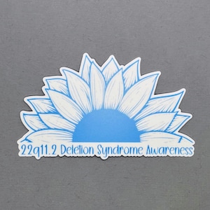May include: A blue and white sunflower sticker with the text "22q11.2 Deletion Syndrome Awareness".