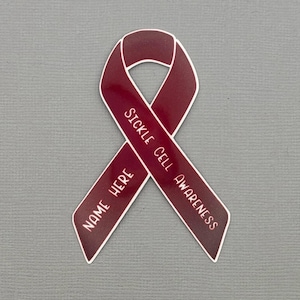 May include: A maroon awareness ribbon with white text that reads "Sickle Cell Awareness" and "Name Here". The ribbon is a symbol of support and advocacy for those affected by sickle cell disease.