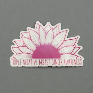 May include: A sticker featuring a pink and white sunflower design. The center of the flower is a solid pink, with white petals radiating outwards. The text "TRIPLE NEGATIVE BREAST CANCER AWARENESS" is printed below the flower.