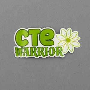 May include: A sticker with the words "CTE WARRIOR" in green, outlined in white. A white and green daisy is on the right side of the sticker. The sticker is on a gray background.