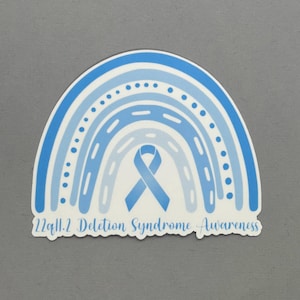 May include: A blue and white rainbow sticker with a blue ribbon in the center. The text "22q11.2 Deletion Syndrome Awareness" is at the bottom of the sticker.