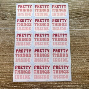 May include: A sheet of 18 pink and white stickers with the text "Pretty Things Inside" repeated on each sticker.