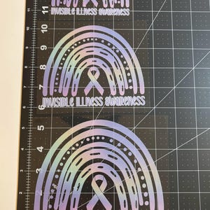 May include: Three rainbow-shaped stickers with the text "INVISIBLE ILLNESS awareness". The stickers have a gradient color scheme of light blue, purple, and yellow. Each sticker features a ribbon symbol.