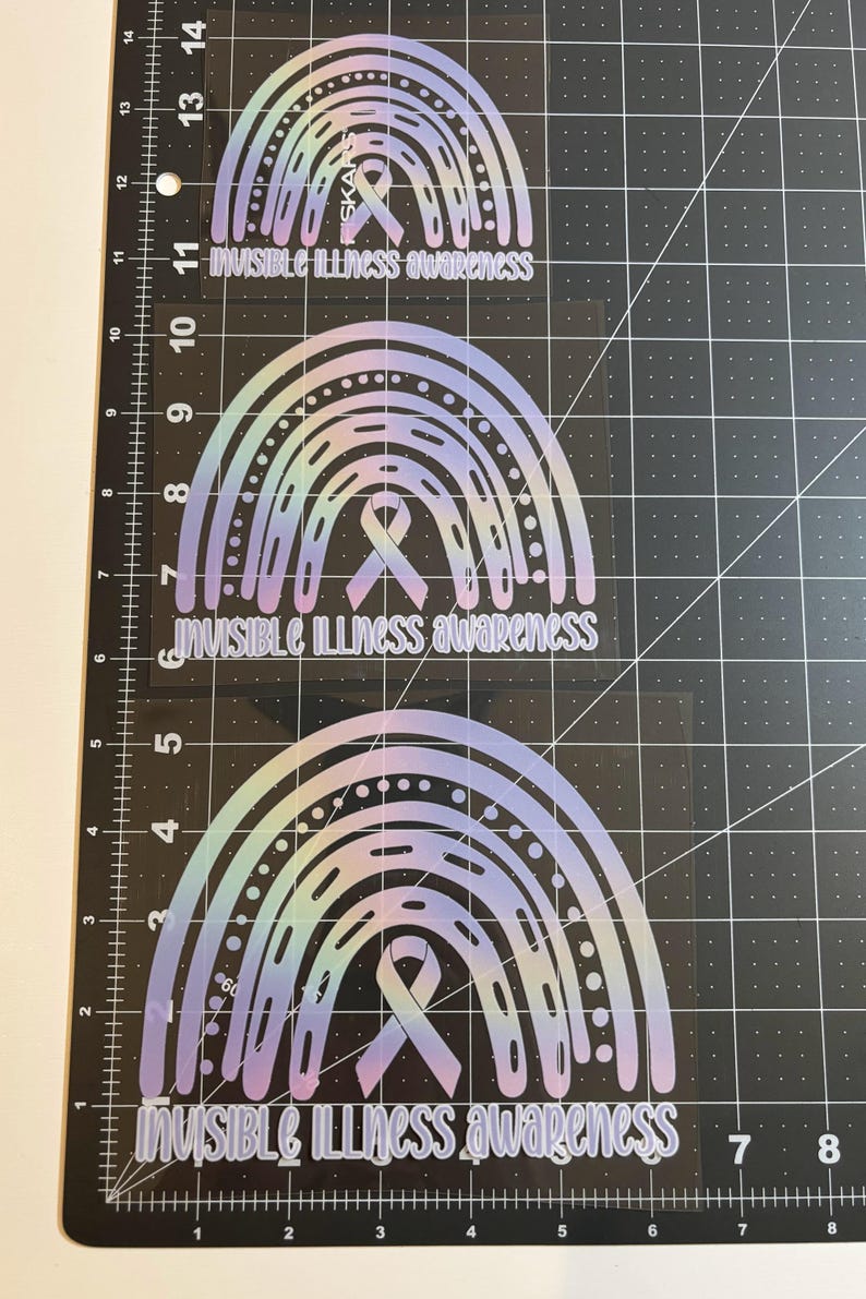 May include: Three rainbow-shaped stickers with the text "INVISIBLE ILLNESS awareness". The stickers have a gradient color scheme of light blue, purple, and yellow. Each sticker features a ribbon symbol.