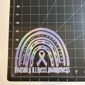 May include: A holographic rainbow sticker with the text "INVISIBLE ILLNESS awareness". The design features a rainbow with a ribbon in the center, set against a black grid background.