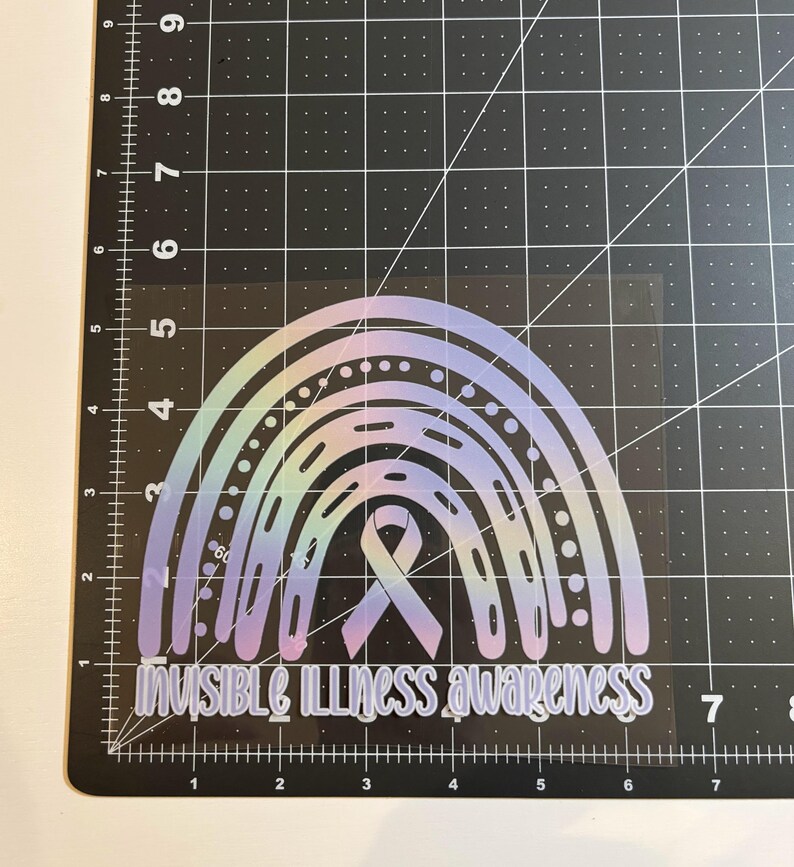 May include: A holographic rainbow sticker with the text "INVISIBLE ILLNESS awareness". The design features a rainbow with a ribbon in the center, set against a black grid background.