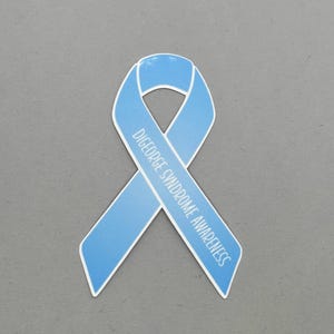 May include: A light blue awareness ribbon with white trim. The ribbon is in the shape of a loop with the words "DiGeorge Syndrome Awareness" printed in white. The ribbon is on a gray background.