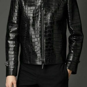 Może przedstawiać: Czarna skórzana kurtka z krokodylim wzorem. Kurtka ma zamek błyskawiczny i stójkę.
