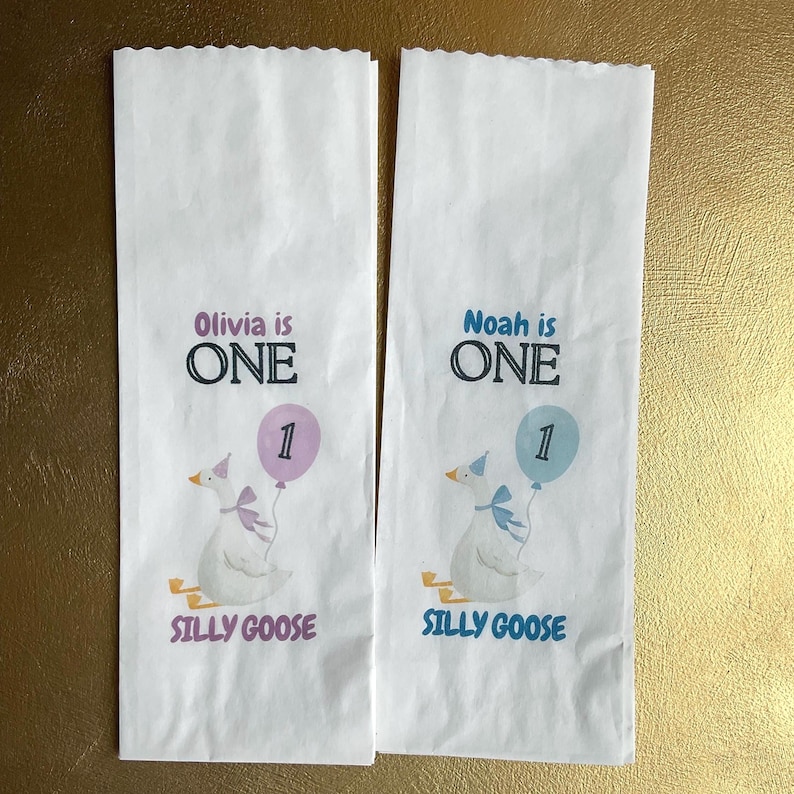 It displays two white rectangular items featuring a goose illustration, the text Olivia is ONE or Noah is ONE, a balloon with the number 1, and the words SILLY GOOSE. One Silly Goose Birthday Girl Personalize Silverware Bag Boy Baby 1st Birthday Favor Custom Cutlery Bag Table Decor Paper Napkin Holder Idea