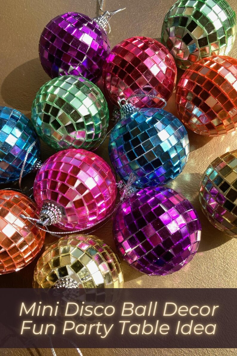 Op de afbeelding: Een verzameling kleine, bolvormige discobalornamenten bedekt met reflecterende, veelkleurige vierkante spiegeltjes in tinten paars, roze, blauw, groen, oranje en goud, elk voorzien van een zilveren ophanglus aan de bovenzijde.