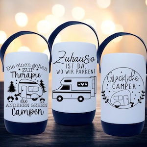 Peut inclure: Trois lanternes de camping blanches avec des poign&eacute;es et des bases noires. Chaque lanterne pr&eacute;sente un motif graphique et textuel noir diff&eacute;rent. L'une dit "Die einen gehen zur Therapie, die anderen gehen Campen". Une autre dit "Zuhause ist da, wo wir parken!" La troisi&egrave;me dit "Gl&uuml;ckliche Camper".