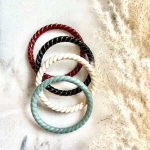 Peut inclure: Quatre bracelets rigides avec une bordure dorée. Les bracelets sont rouge, noir, blanc et bleu clair.