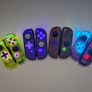 May include: Five different colored Nintendo Switch Joy-Con controllers. The controllers are all in pairs and are lit up with different colors. The colors are green, purple, brown, blue, and red.