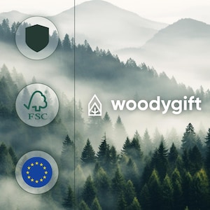 May include: Image featuring a misty forest scene with the text "woodygift" in white. The image also includes the FSC logo, a shield, and the EU flag. The background shows a dense forest with a foggy atmosphere.
