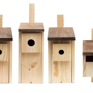 Op de afbeelding: Vier houten vogelhuisjes in verschillende maten, allemaal met een bruin dak en een natuurlijke houten afwerking. De vogelhuisjes hebben een ronde opening waar vogels doorheen kunnen.