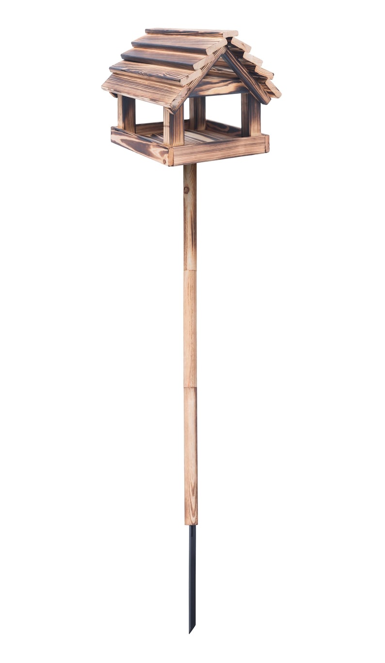 May include: A wooden birdhouse with a peaked roof and open sides, mounted on a wooden pole with a metal stake for ground placement. The birdhouse is made of stained wood, creating a rustic aesthetic.