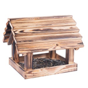May include: A wooden bird feeder with a pitched roof, filled with sunflower seeds. The feeder has a natural wood grain finish with darker, burnt-looking accents. The design is reminiscent of a small house.
