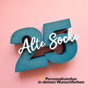 Könnte beinhalten: Eine dreidimensionale Zahl 25 in Petrol mit dem weißen, kursiven Schriftzug Alte Socke darauf. Unter der Zahl steht in schwarzer Schrift Personalisierbar in deinen Wunschfarben, ergänzt durch ein kleines gelbes vierzackiges Sternsymbol.