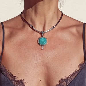 May include: A silver choker necklace with a turquoise stone pendant. The necklace is made of leather and has a silver bar with decorative accents.