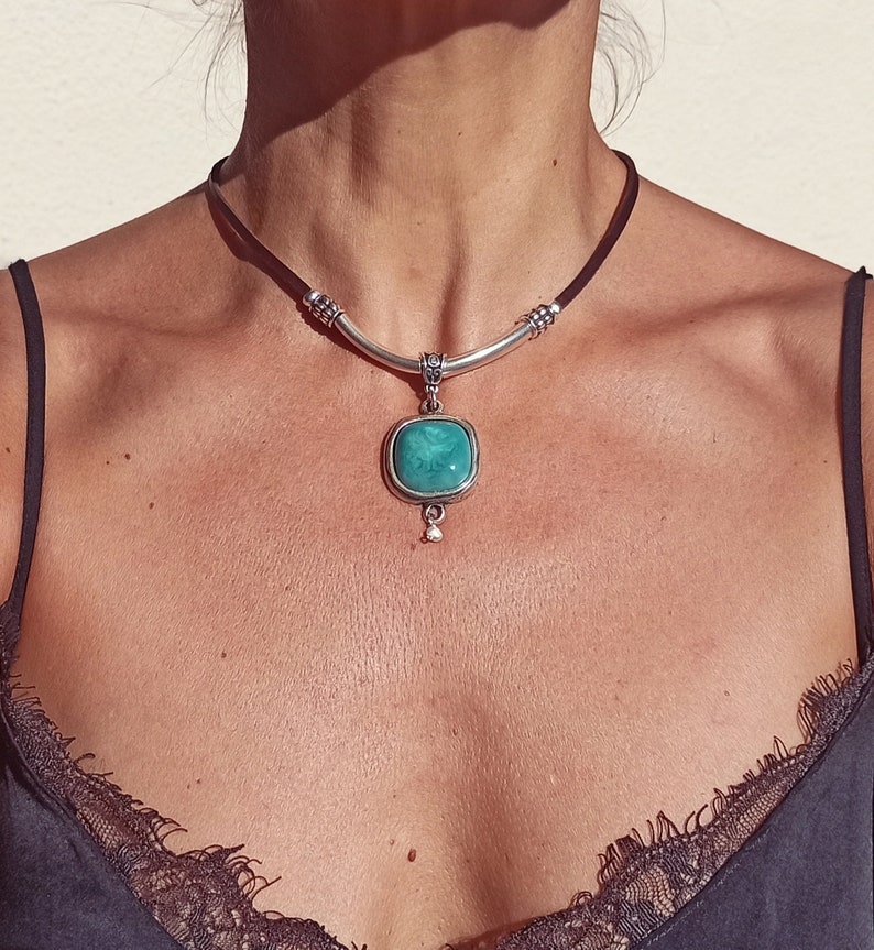 May include: A silver choker necklace with a turquoise stone pendant. The necklace is made of leather and has a silver bar with decorative accents.