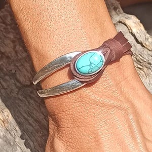 May include: A brown leather bracelet with a silver cuff and a turquoise stone. The cuff has a hammered texture.